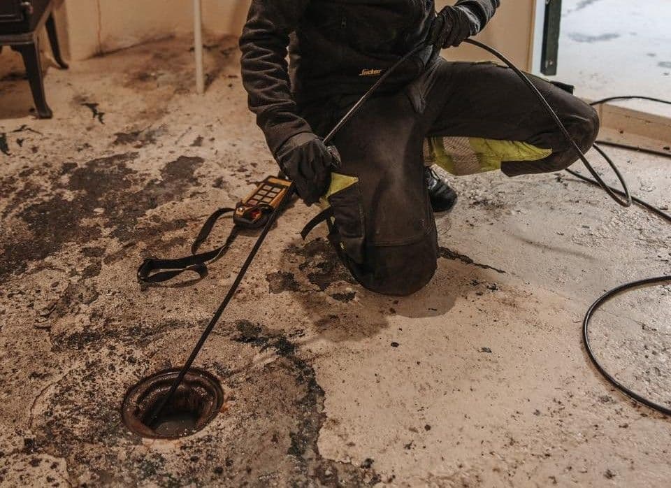 Bilde som viser Spylespesialist som spyler avløpsrør via sluk i kjeller